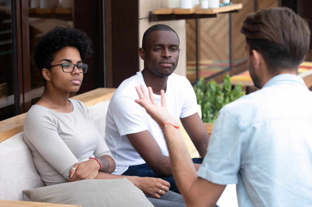 Bored Serious Black Married Couple Sitting Together on Couch Visiting Medical Specialist Listening Psychologists Counselor Feeling Disinterested and Mistrust to Methods of Psychological Assistance